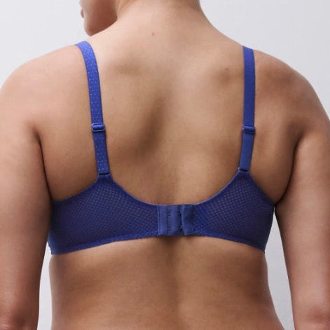 A woman shown from the back wearing a blue mesh underwire bra with adjustable shoulder straps and a center back strap detail, against a plain light gray studio background.