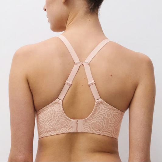 Woman wearing a beige lace bralette against a plain background