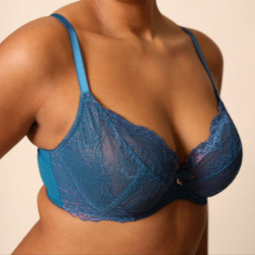 Woman wearing a blue lace bra against a beige background