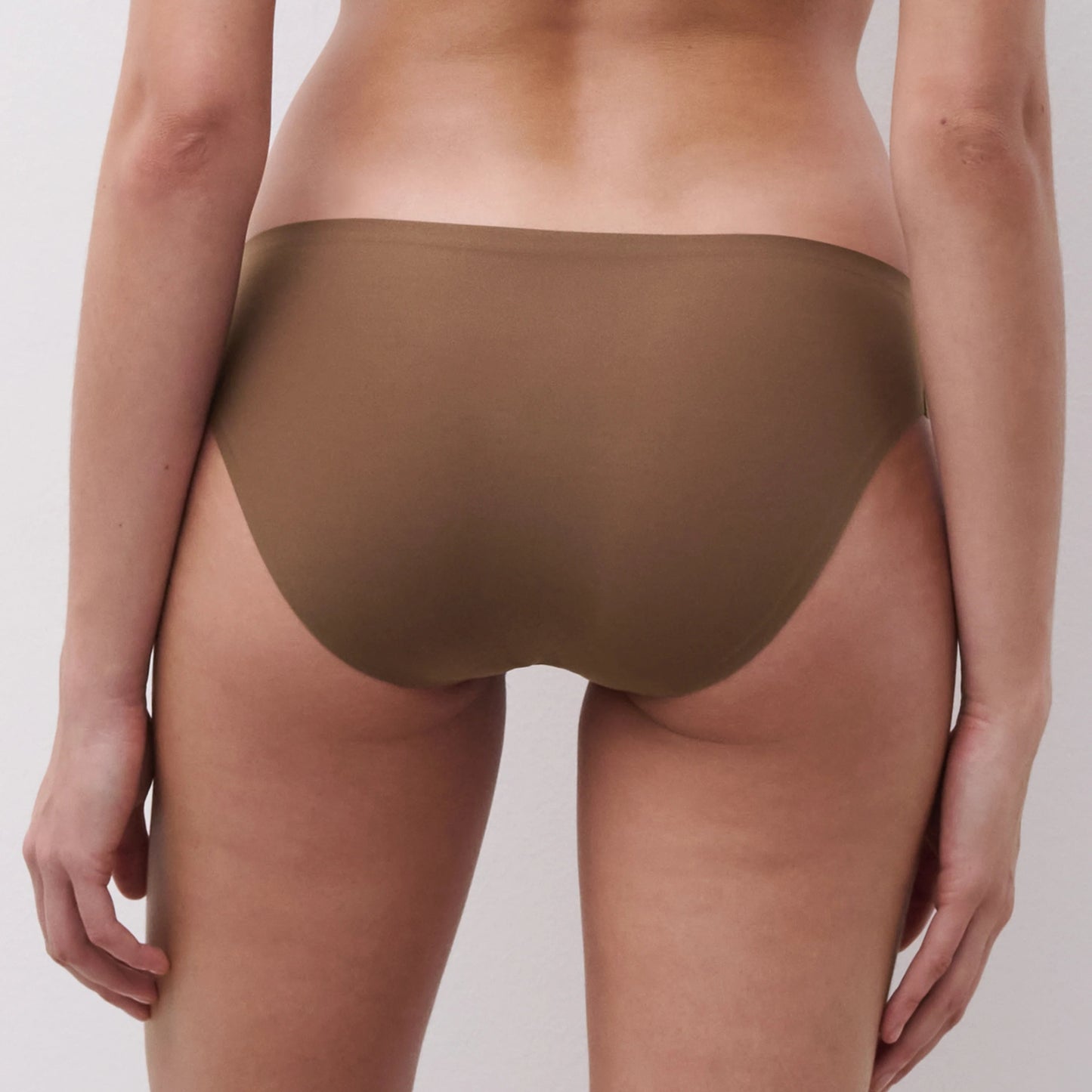 Rear view of a model wearing a pair of solid brown underwear against a light gray studio background.