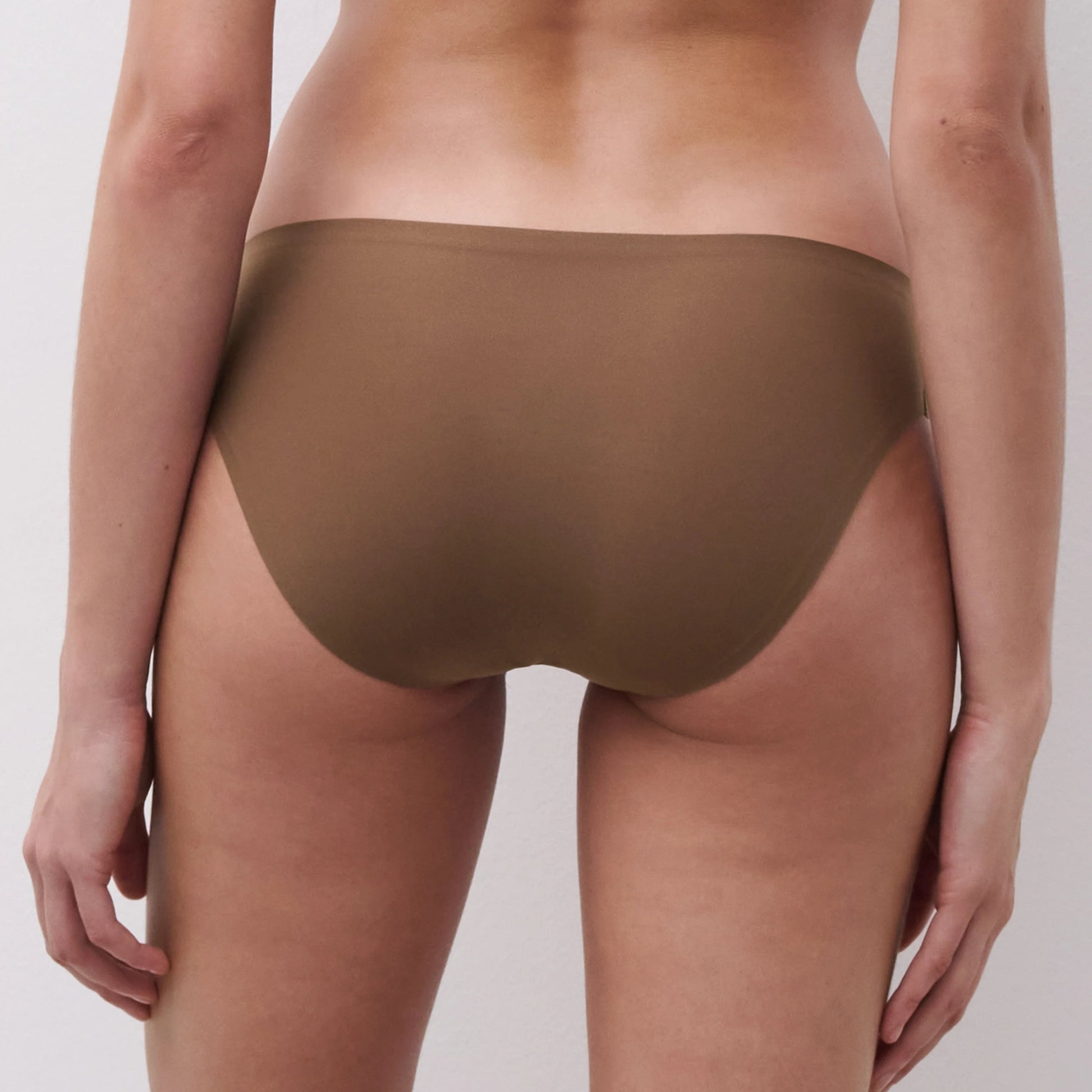 Rear view of a model wearing a pair of solid brown underwear against a light gray studio background.