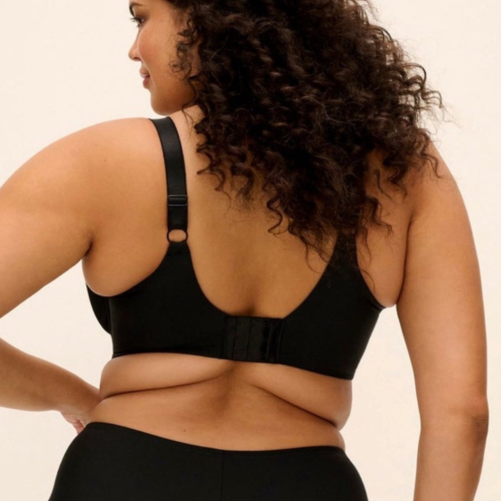 A woman shown from the back wearing a black bralette and matching high-waisted briefs against a plain light beige studio background.