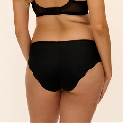 A woman shown from the back wearing a black sheer mesh bralette and matching black high-waisted briefs with scalloped edges, against a plain light beige studio background.