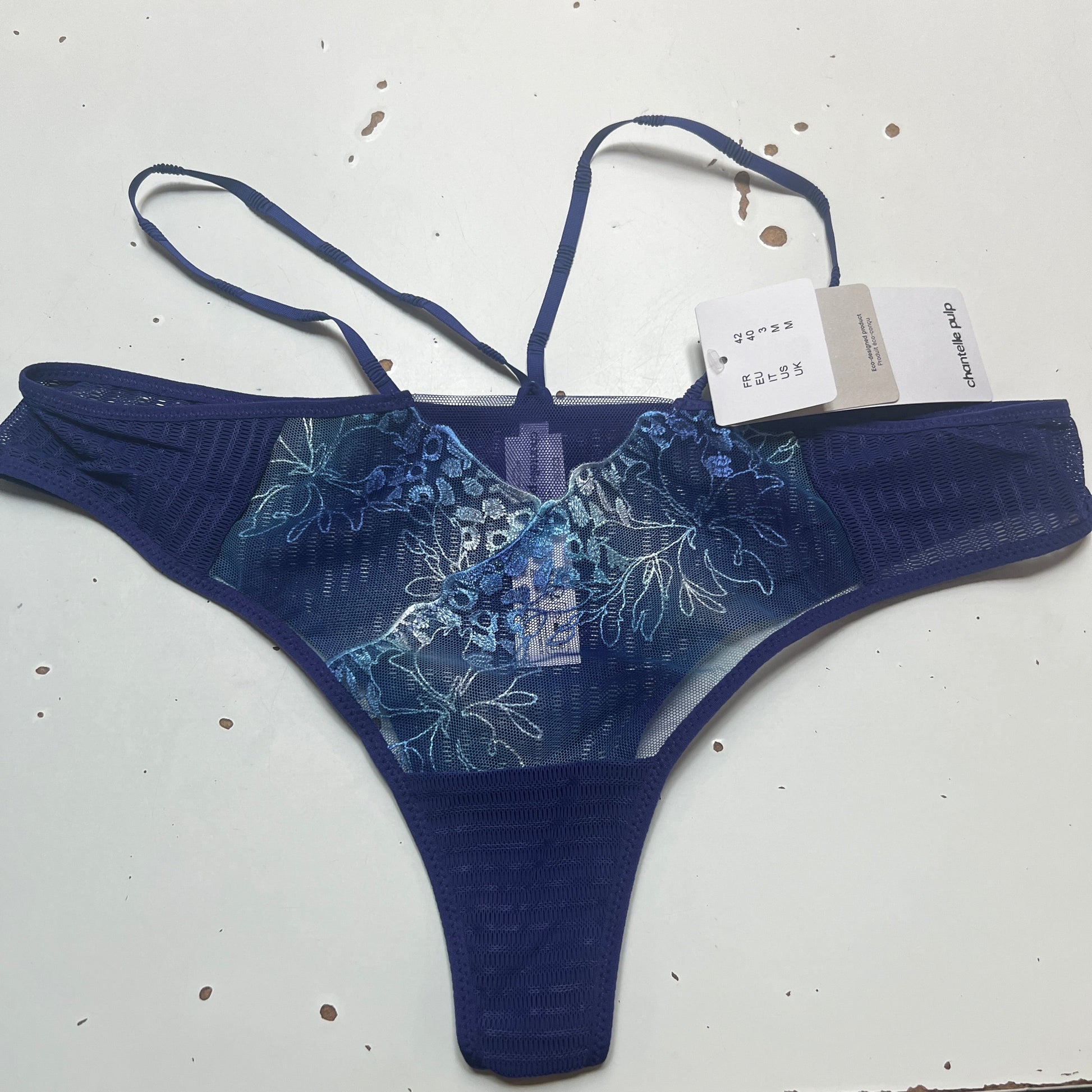 Blue floral-patterned THONG on a white surface with a visible tag.
