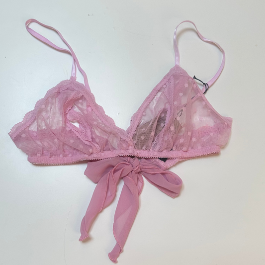 A pink sheer mesh bralette with lace cups, thin adjustable straps, and a matching fabric bow at the center front, laid flat on a white surface.