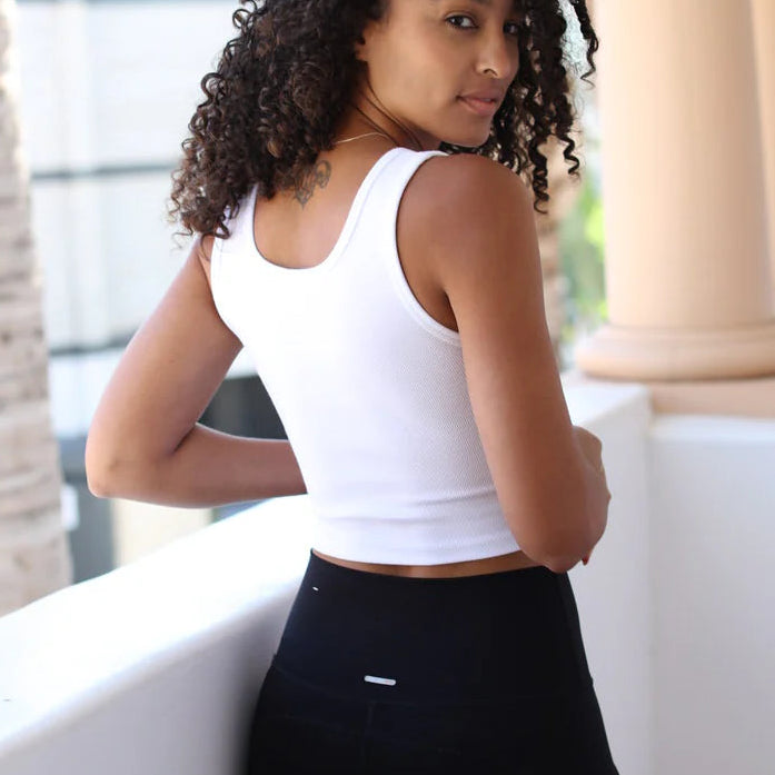 Woman wearing a white tank top and black pants standing in front of architectural columns.