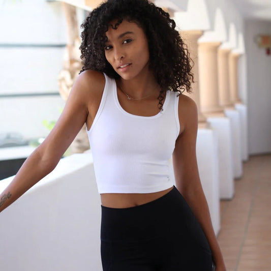 Woman wearing a white tank top and black pants in an outdoor setting