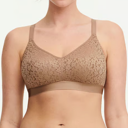 Woman wearing a beige lace bralette against a plain background