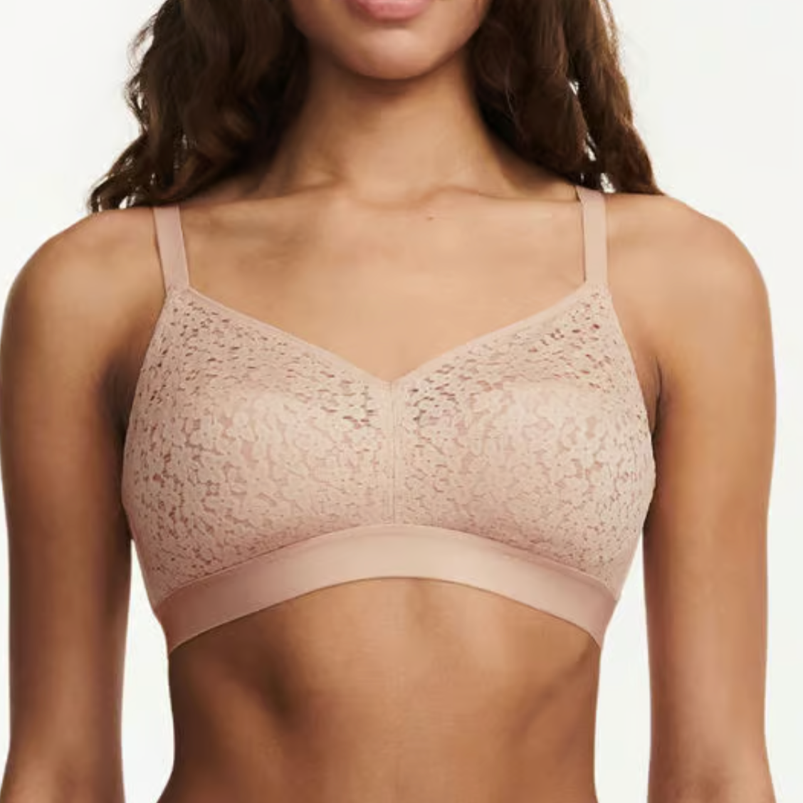 Woman wearing a beige lace bralette against a plain background
