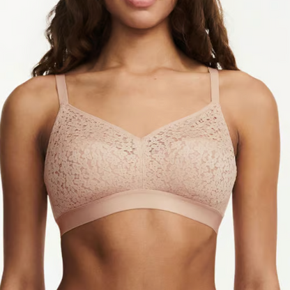 Woman wearing a beige lace bralette against a plain background