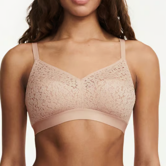 Woman wearing a beige lace bralette against a plain background