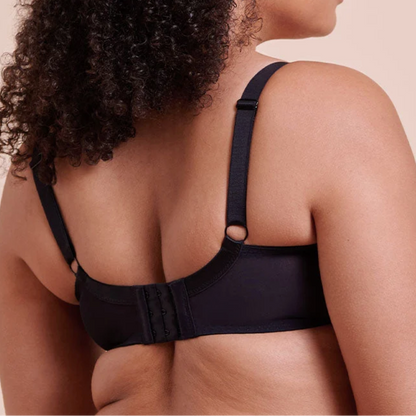 A woman shown from the back wearing a black bra with adjustable straps and a hook-and-eye closure, against a solid beige background.