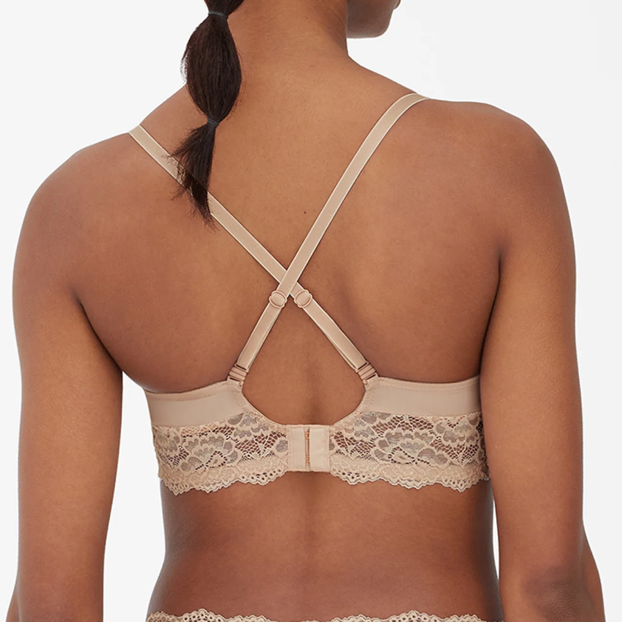 Rear view of a woman wearing a beige lace bra with crisscross back straps, shown against a plain light background.