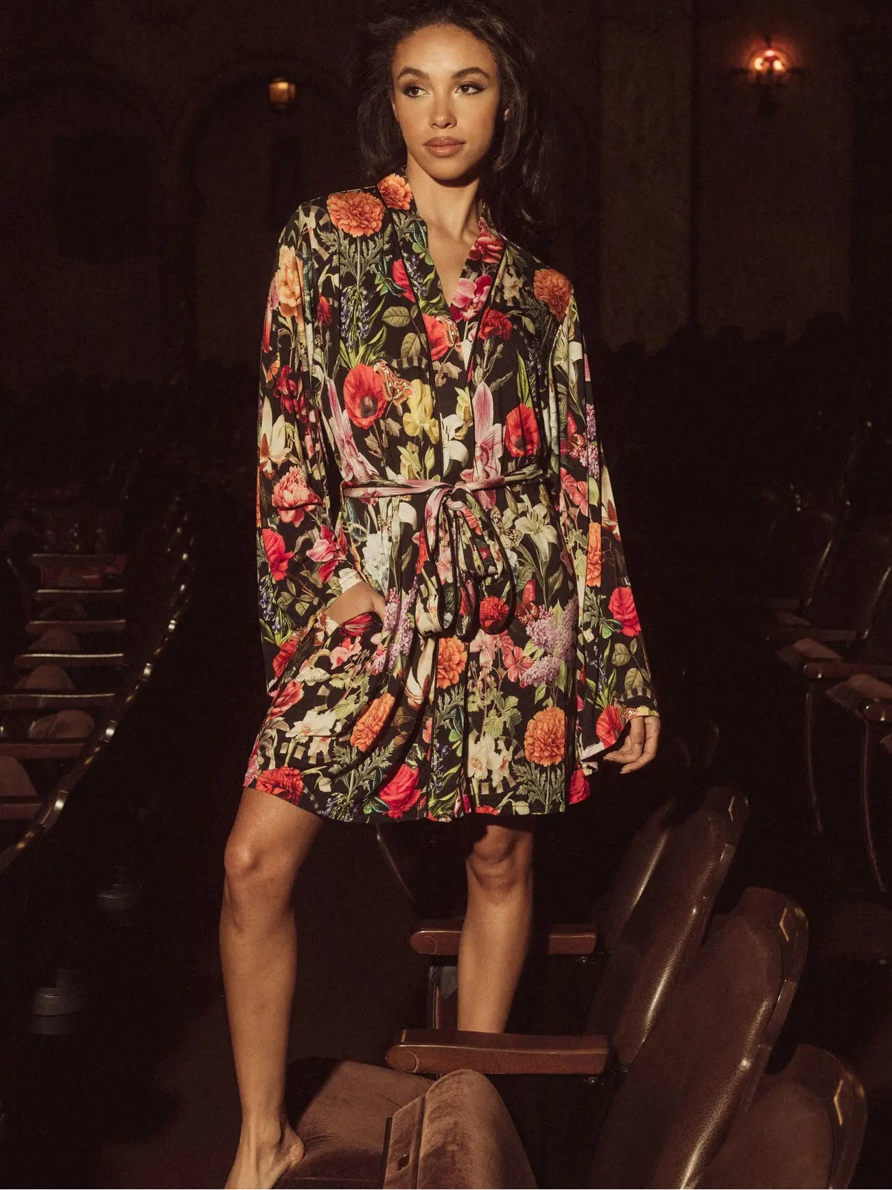 Woman in a floral robe standing in an auditorium with dark seats.